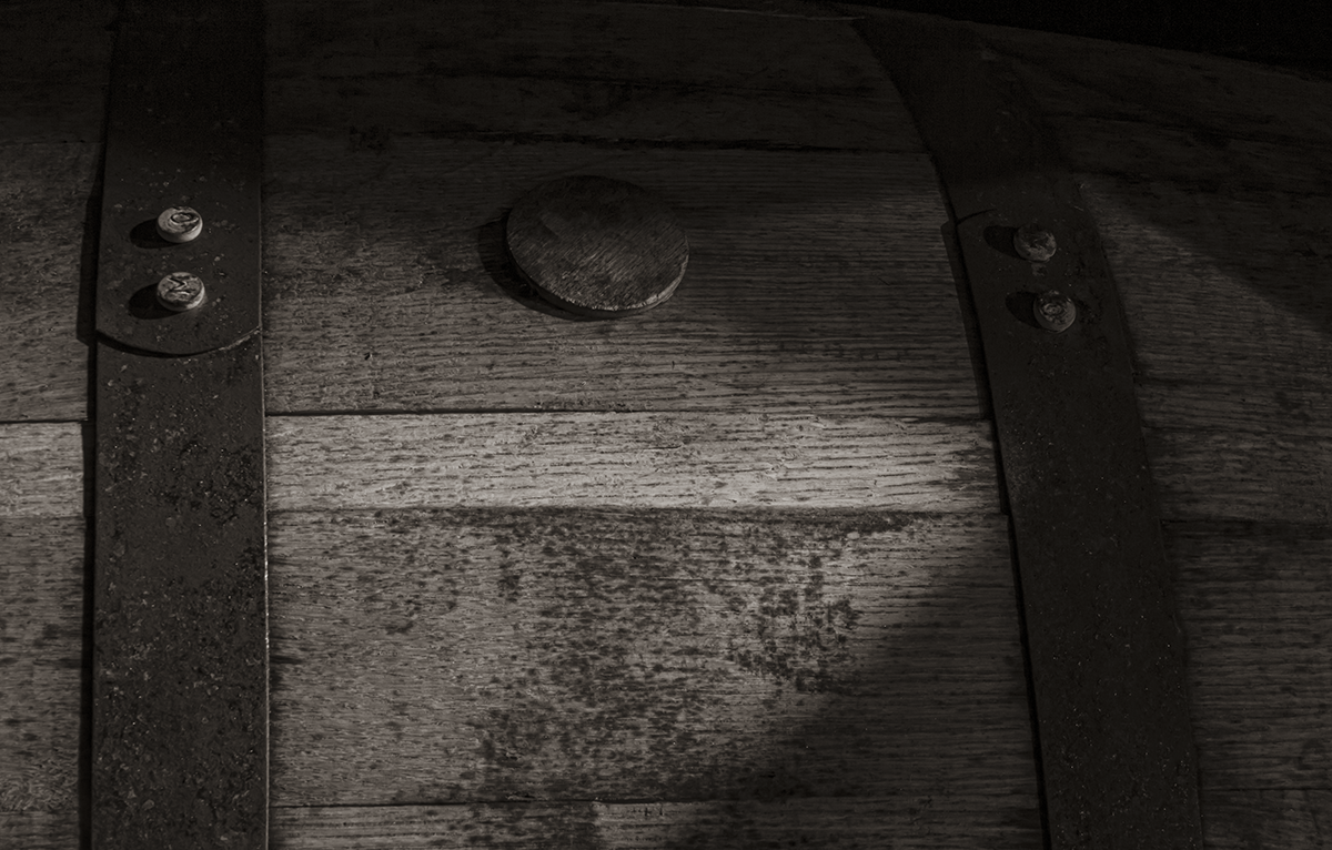 A black and white image of a whiskey barrel maturing in a dark rickhouse. Photo ©2019, Mark Gillespie/CaskStrength Media.